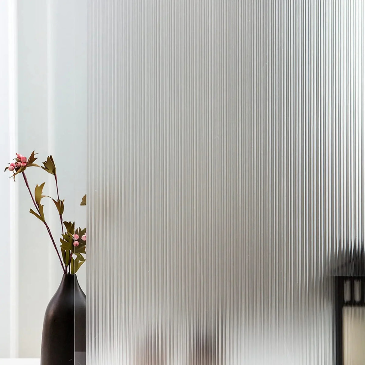 A dark vase with pink flowers sits in front of a white wall with vertical frosted stripe privacy film.