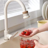 A hand is using a kitchen faucet sprayer to dispense water onto fresh tomatoes in a glass.