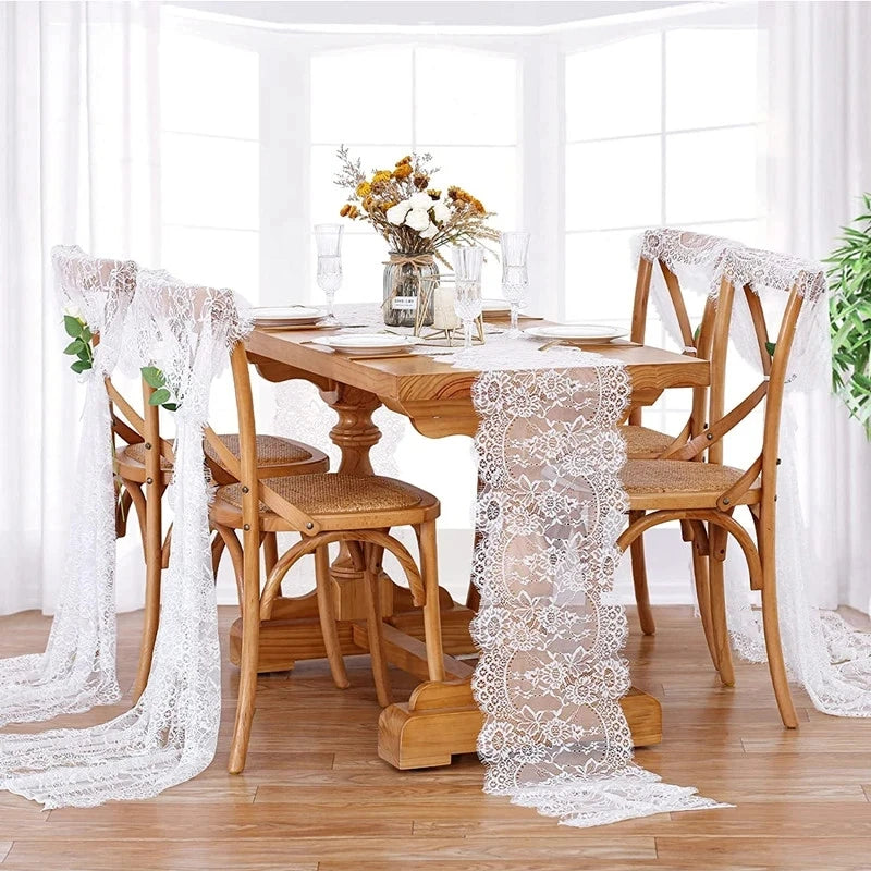 A wooden dining table set for a meal with an embroidered floral lace table runner and white sheer fabric on a bright windowsi