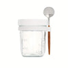 A clear glass jar with a white lid and a wooden spoon resting on top.