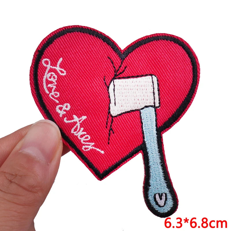 A red heart shaped iron-on patch embroidered with the text Love & Trust and a white iron tool.