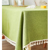 A lime green linen tablecloth with white tassels draped over a wooden table.