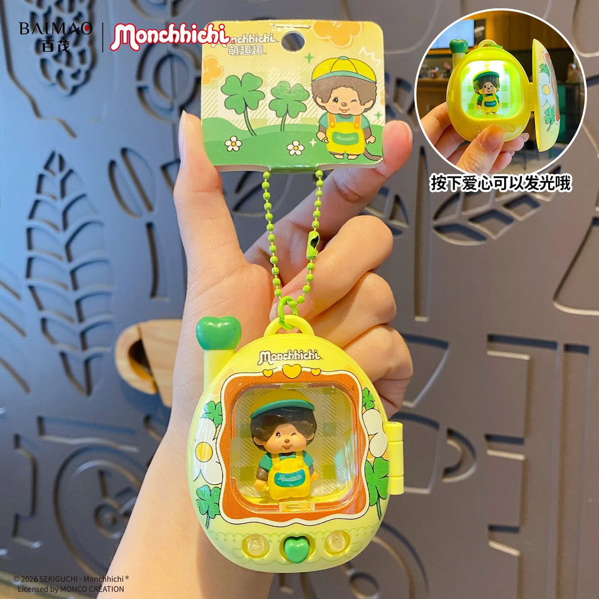 Une main tient un porte-clés de sac à dos en carton jaune avec une silhouette lumineuse à l'intérieur, au design vert et jaun