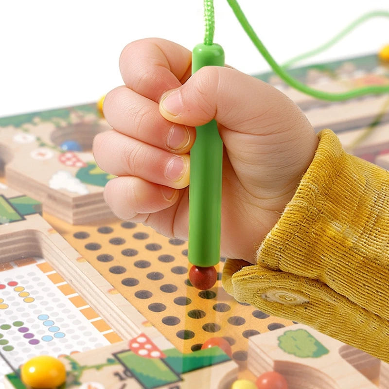 A hand holds a green magnetic color sorting maze board with a peg, demonstrating a Montessori wooden learning toy.