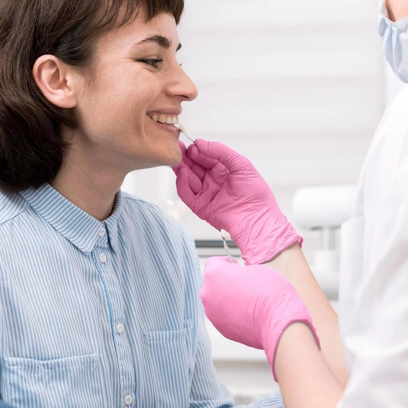 A woman in a striped shirt is being fitted with pink nitrile disposable gloves by another person.
