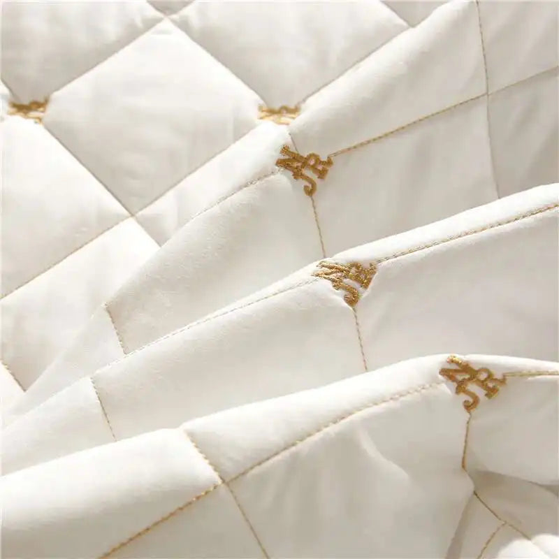 Close-up of a white quilted bed skirt featuring gold embroidery on the fabric.