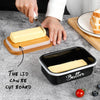 A black metal butter dish with a lid and a stainless steel knife is shown on a gray surface.