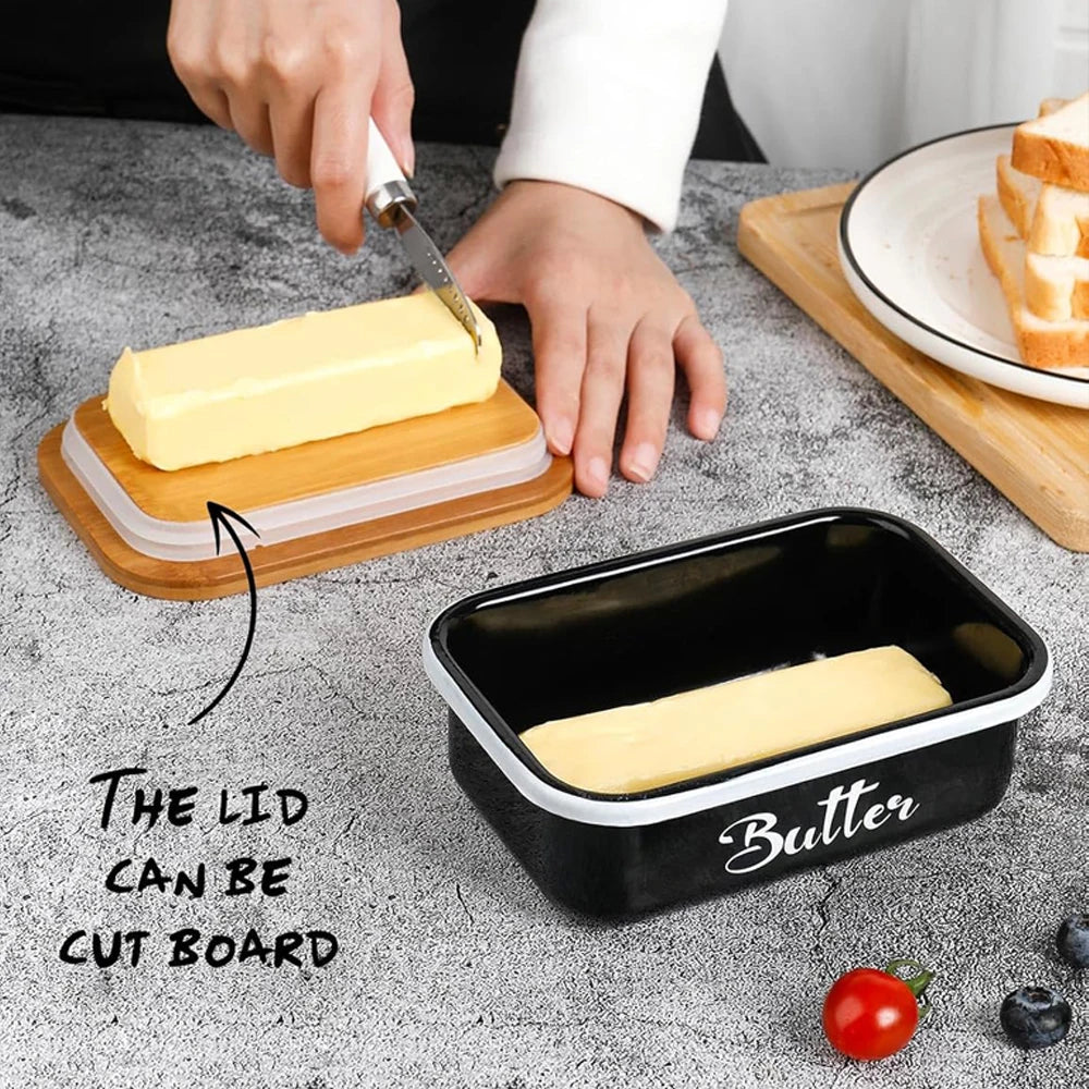 A black metal butter dish with a lid and a stainless steel knife is shown on a gray surface.