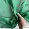 A close-up of a sheer, light green silk chiffon fabric draped and folded by a hand.