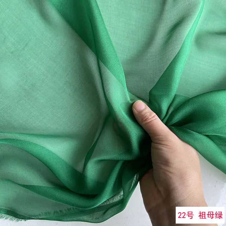 A close-up of a sheer, light green silk chiffon fabric draped and folded by a hand.