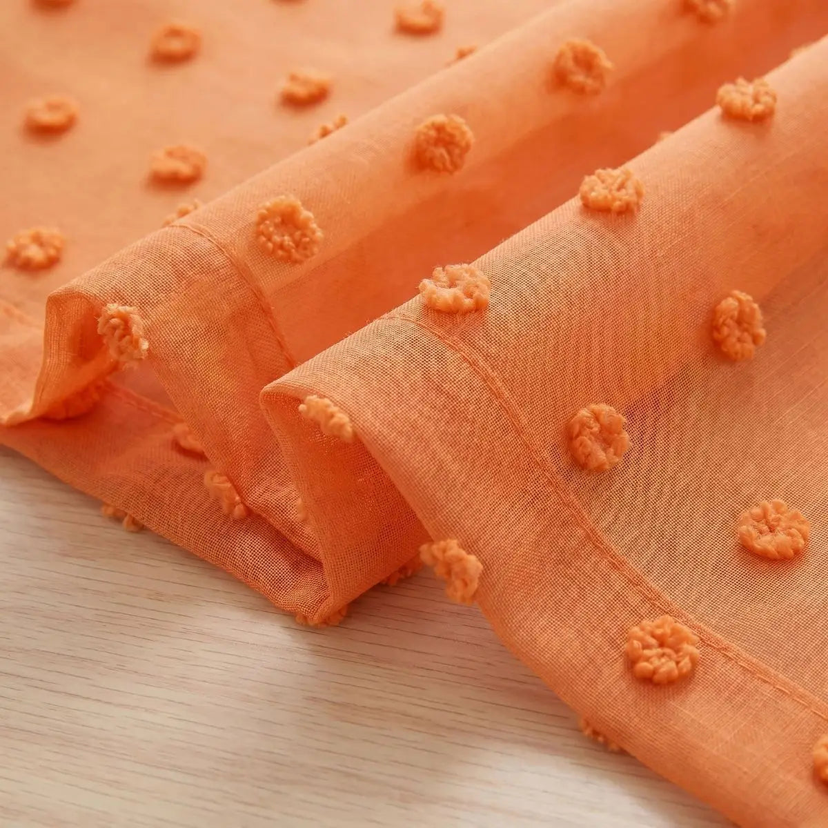 Orange sheer curtains featuring pom pom details and a 3D jacquard rod pocket.
