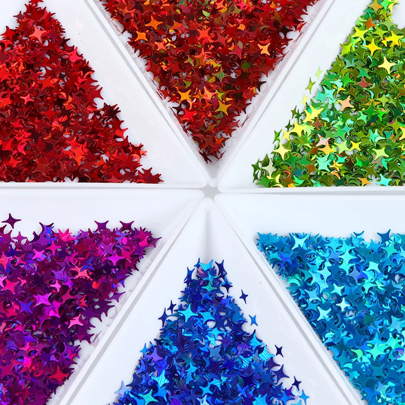 A collection of shiny holographic star sequins in various colors like red, green, purple, and blue arranged in a white box.