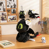 A black soft plush dragon toy resembling a Night Fury, displayed among framed artwork.