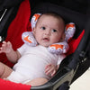 A baby is seated in a black car seat with an orange and white patterned head and neck support pillow.