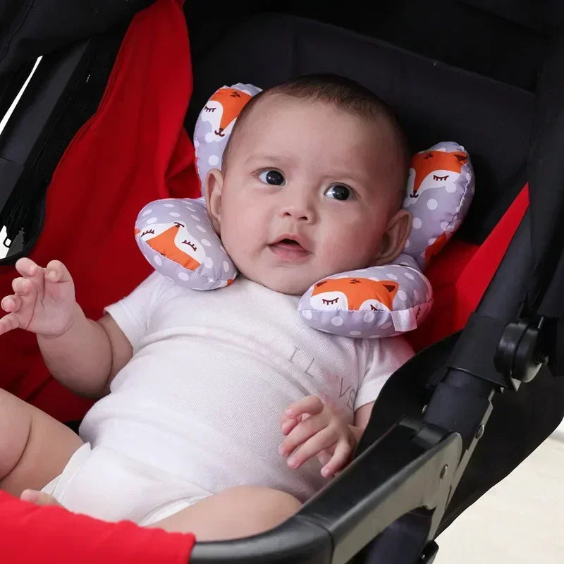 A baby is seated in a black car seat with an orange and white patterned head and neck support pillow.