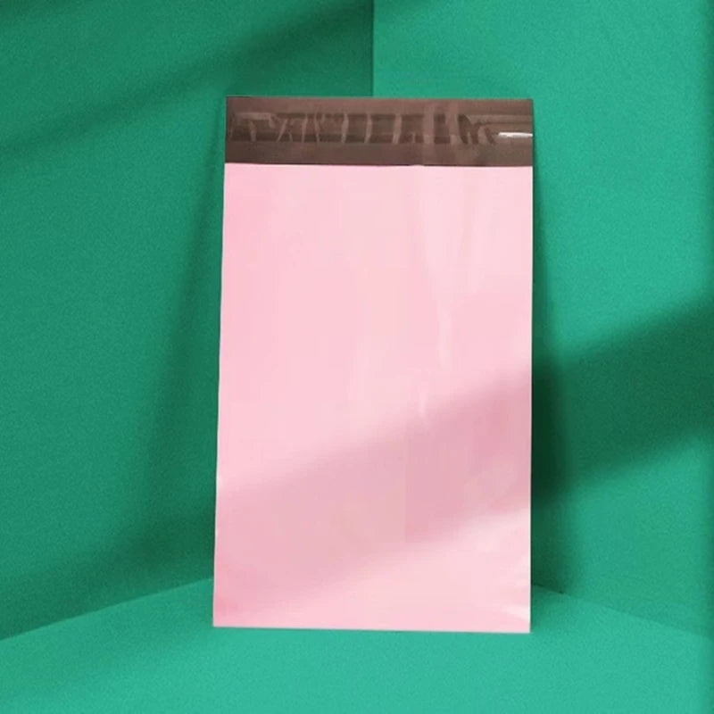 A vertical pink waterproof poly mailer shipping bag with a brown top, set against a green background.