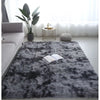 A gray luxury velvet plush carpet placed in a bright living room with a potted plant and natural light.