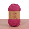 A skein of magenta crochet yarn is displayed on a wooden surface with a brown label.