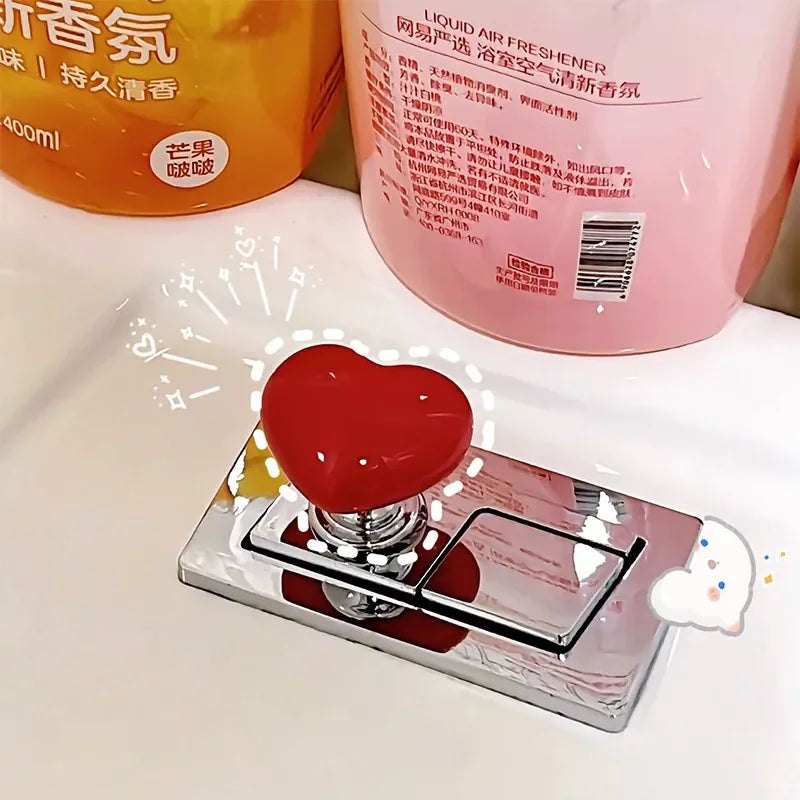 A heart-shaped toilet flush button with a nail protector is displayed on a silver tray.