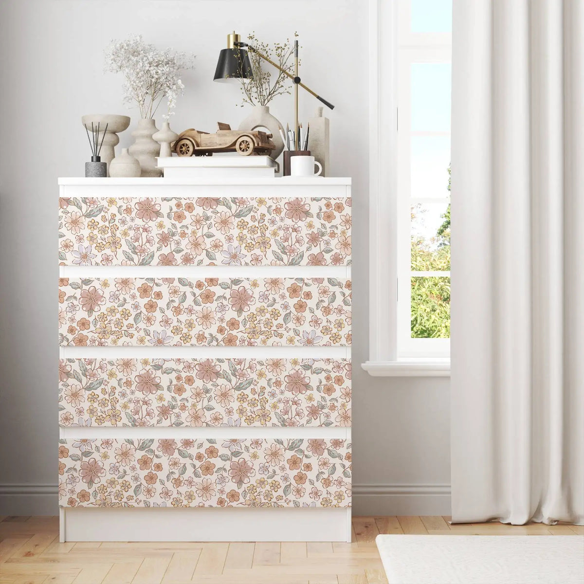 A white cabinet decorated with vintage floral peel-and-stick wallpaper featuring soft pink and green botanical patterns.