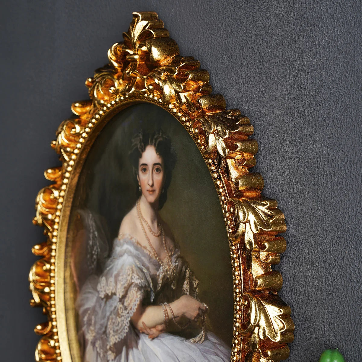 An ornate gold-framed portrait of a woman with dark hair and pearl jewelry.