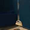 A modern brass broom and dustpan set with a floor wiper resting on a wooden floor.