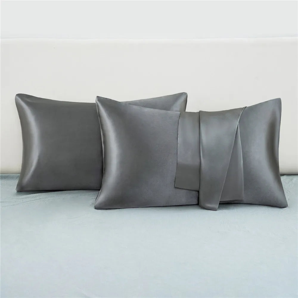 A set of two silky satin pillowcases in a muted gray color are displayed on a light blue bed.
