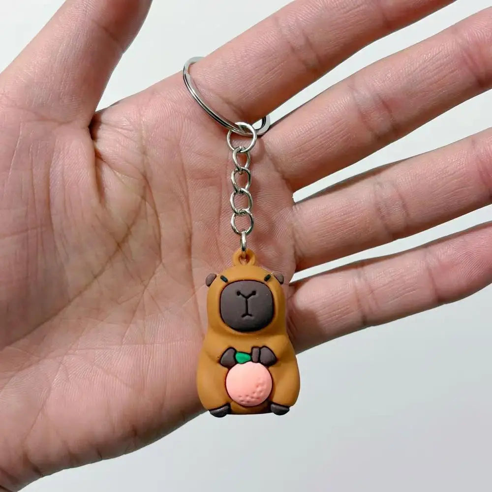 A small brown capybara charm keychain hanging from a silver split ring on a person's hand.