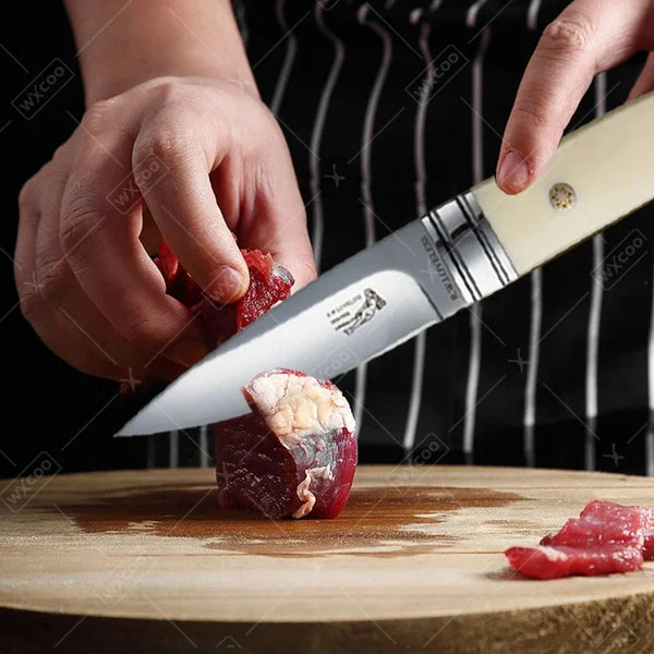 A hand is using a stainless steel chef's cleaver to cut a piece of raw red meat on a wooden cutting board.