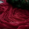 A deep red crinkle gauze cheesecloth table runner draped next to a green festive wreath.