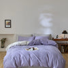 A purple quilted duvet cover set with pillows on a bed in a bright room.