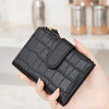 A hand holds a black croc-embossed PU leather bifold wallet.
