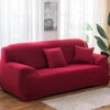 A deep red elastic stretch sofa cover with throw pillows placed in a bright living room.
