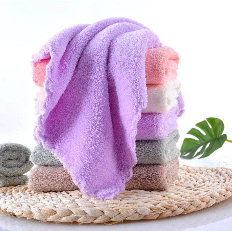A stack of ten ultra-soft coral velvet face towels in various shades of pink and peach resting on a woven mat.