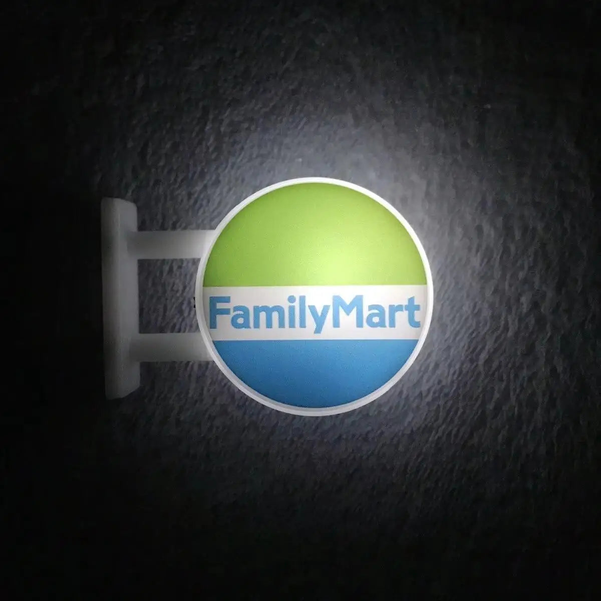 A round magnet featuring the FamilyMart logo with a bright lime green background and blue text on a dark surface.