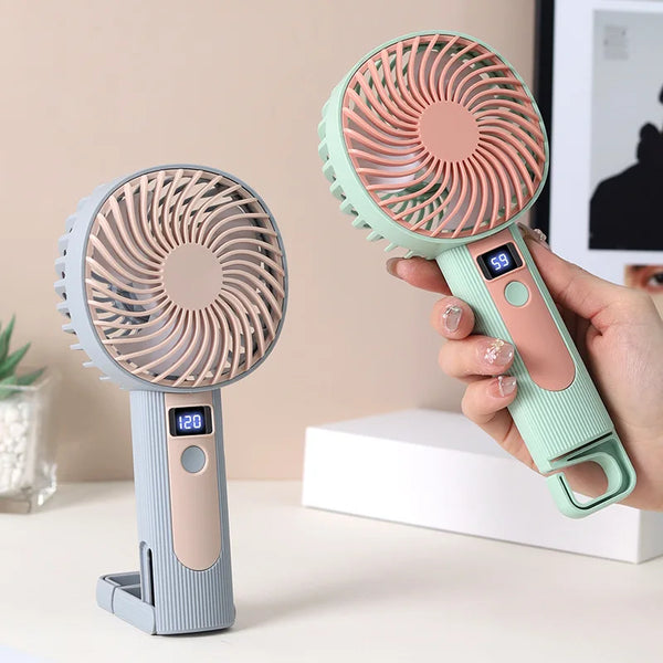 Eine Hand hält einen tragbaren, wiederaufladbaren USB-Ventilator in rosa und mintgrüner Farbgebung.