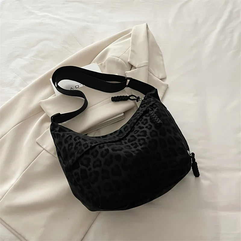 A black leopard print crossbody bag is displayed against a white background with a white blazer.