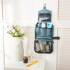 A teal hanging toiletry bag with a waterproof lining is displayed on a white shelf next to a vase of white flowers and skinca