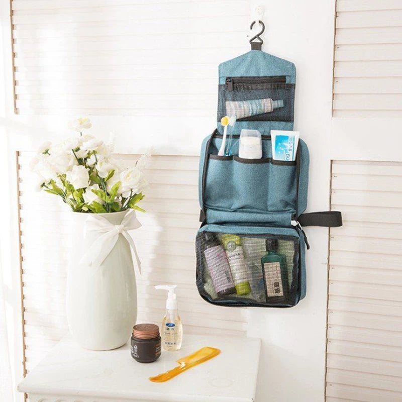 A teal hanging toiletry bag with a waterproof lining is displayed on a white shelf next to a vase of white flowers and skinca