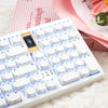 A white mechanical keyboard with light blue backlit keys and a pink background, featuring a cute cat PBT keycap set.