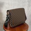A brown patterned crossbody bag with a black strap resting on a wooden table against a gray background.