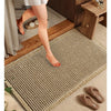 A close-up of a beige waffle weave bath mat with tassels placed on a wooden floor.