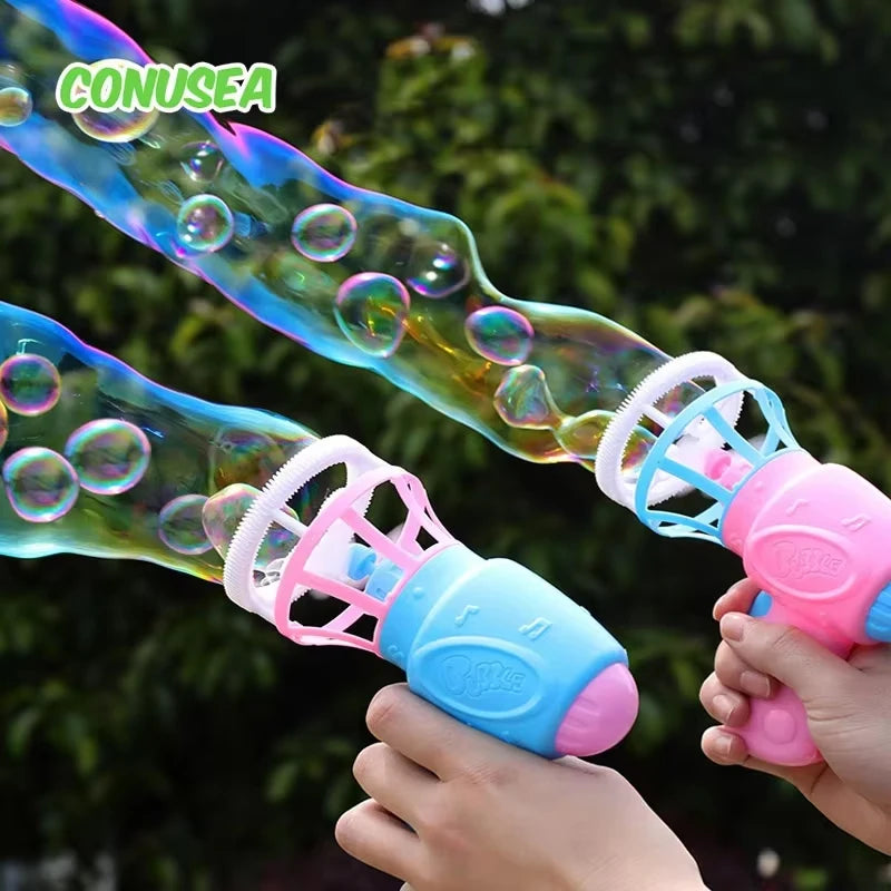 A hand is holding a pink and blue automatic bubble gun with soft fan blades, shooting bubbles against a blurred green backgro