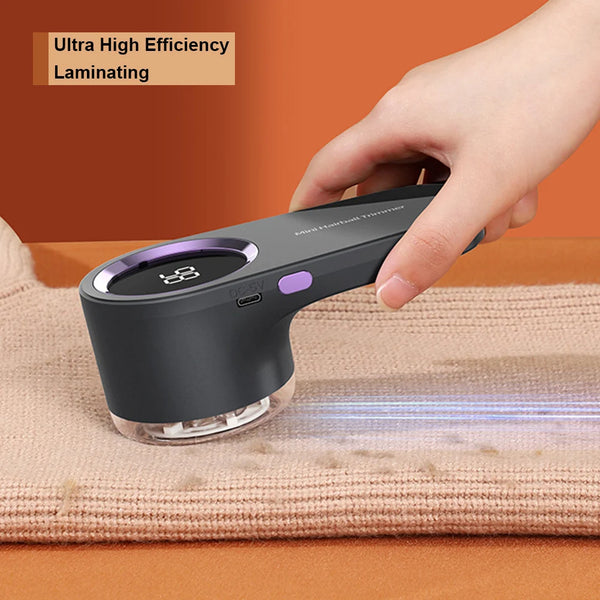 A hand holds a black electric fabric shaver lint remover device, demonstrating its use on a piece of fabric.