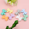 A collection of colorful food-grade silicone crown beads in pastel shades arranged on a pink background.