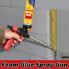 A hand is using a red foam glue spray gun to apply PU foam on a gray wall surface.