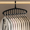 A black clothes hanger with multiple hooks is suspended from a wooden bar, displaying several light-colored shirts.