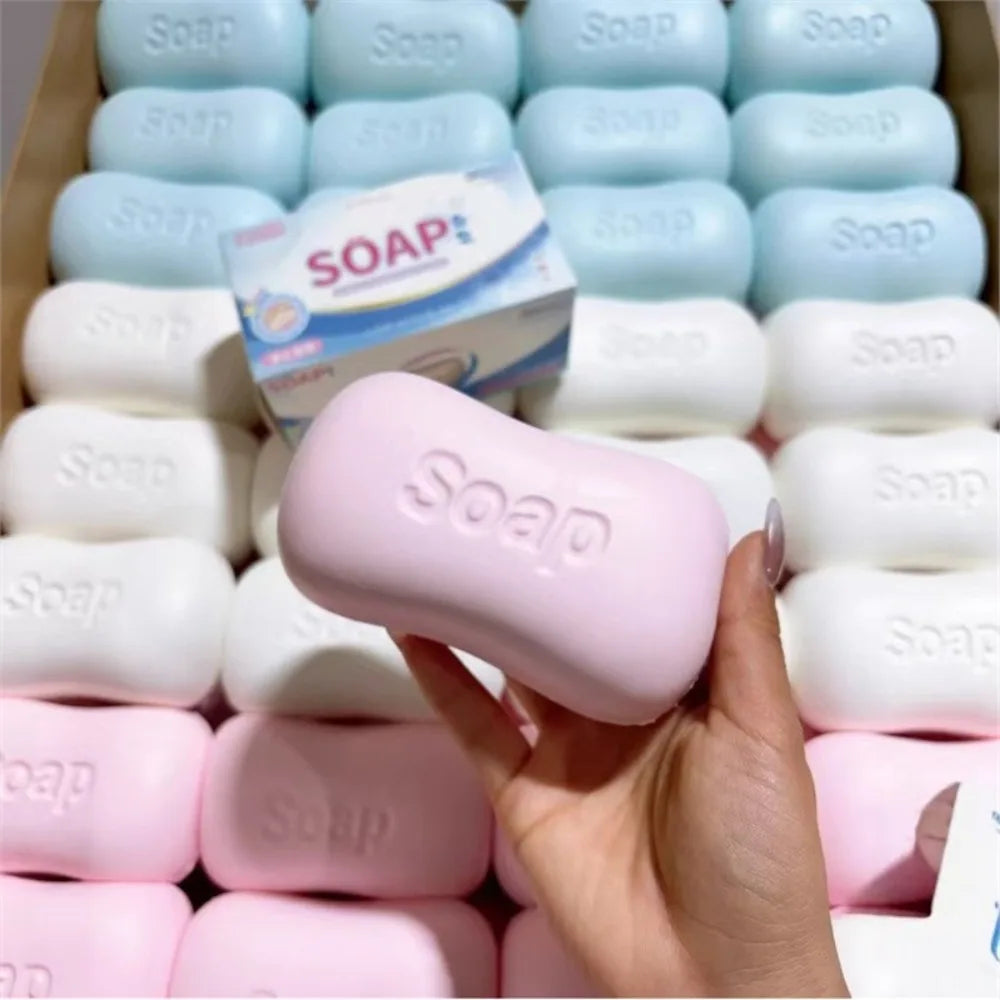 A hand holds a pink stress relief squishy soap shape fidget toy with many white and pink soaps stacked in the background.