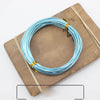 A coil of blue and silver anodized aluminum jewelry wire resting on a wooden board.