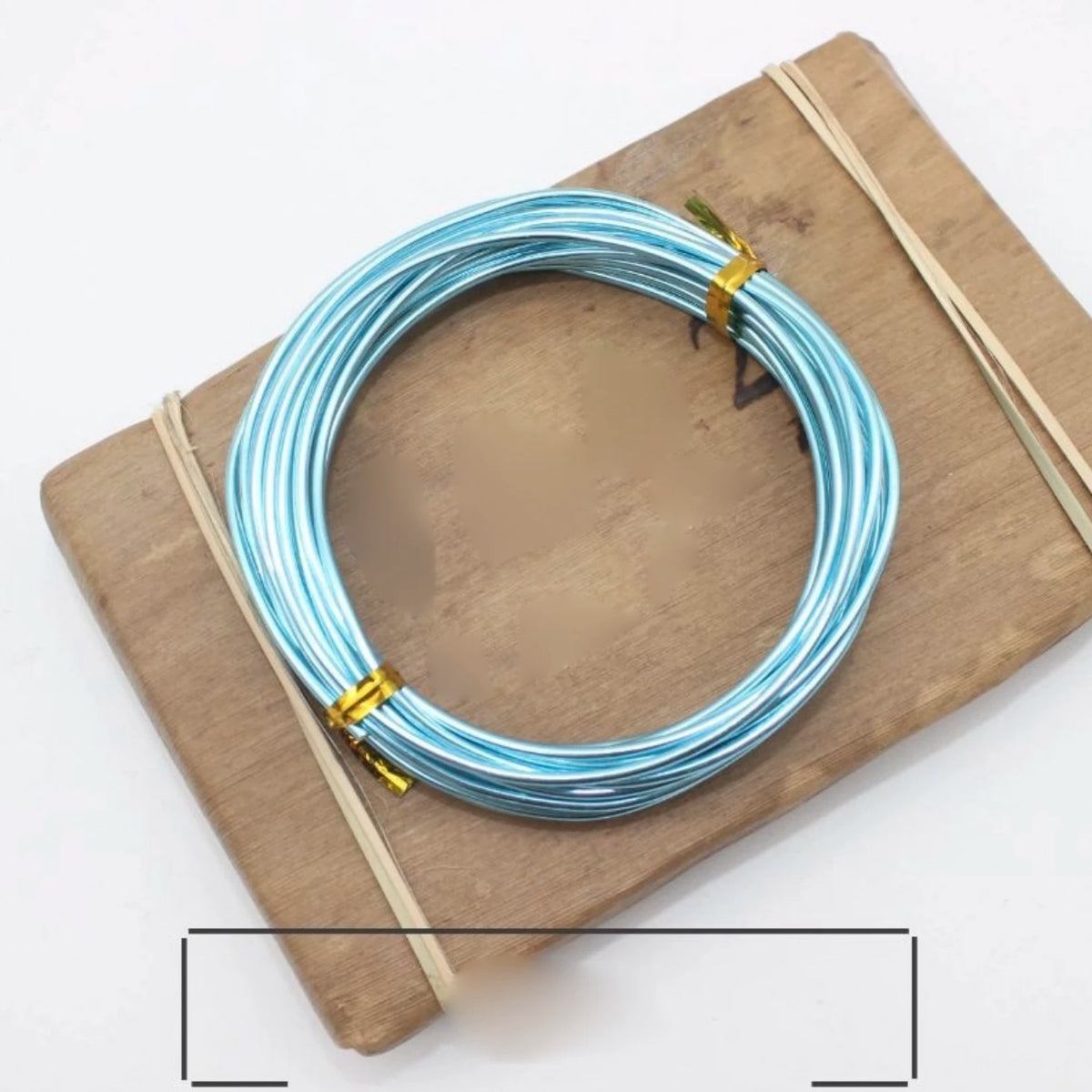 A coil of blue and silver anodized aluminum jewelry wire resting on a wooden board.